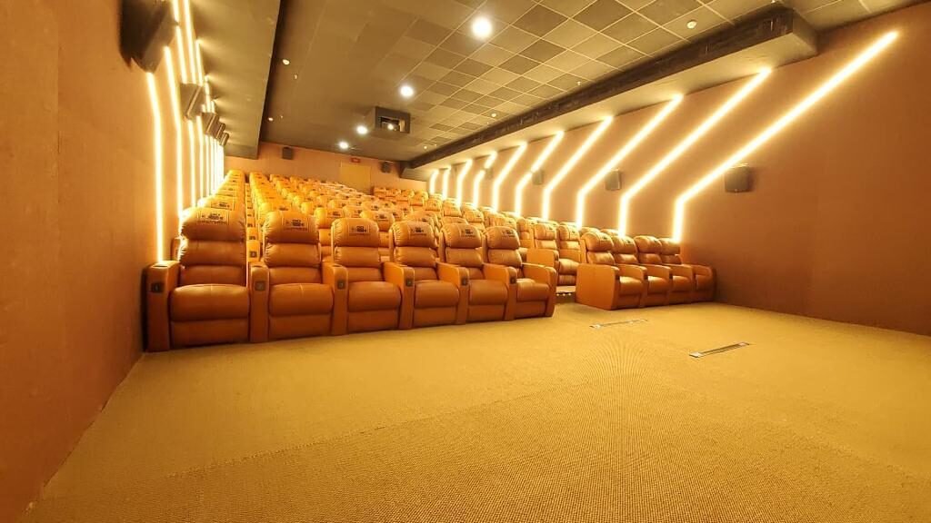 A Cineverse Multiplex auditorium with tan leather recliners and gold chevron wall lighting