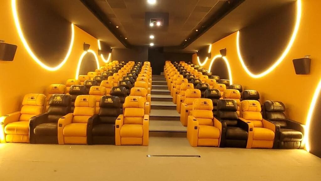 A Cineverse Multiplex auditorium with gold and black recliners beneath glowing halo wall lighting